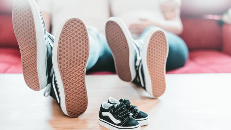 Feet with similar shoes resting on a table. 